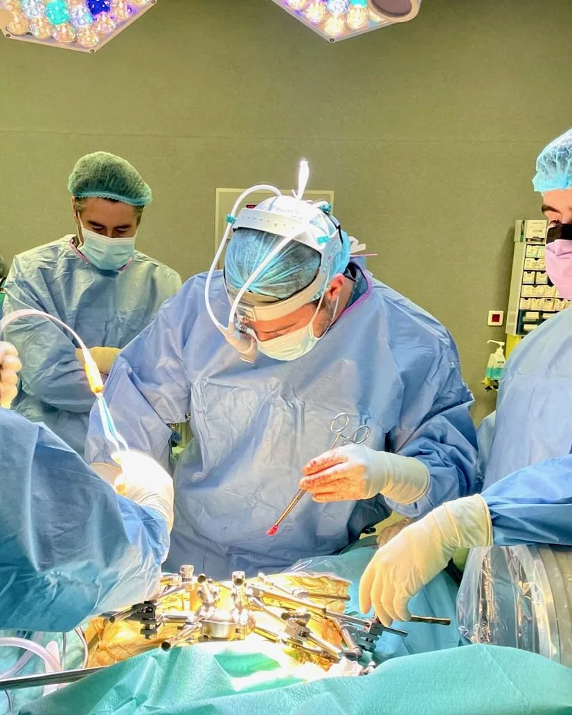 Dr. Rafael Portela e a sua equipa médica realizam uma cirurgia complexa à coluna vertebral, concentrados no campo operatório sob iluminação cirúrgica de alta precisão.