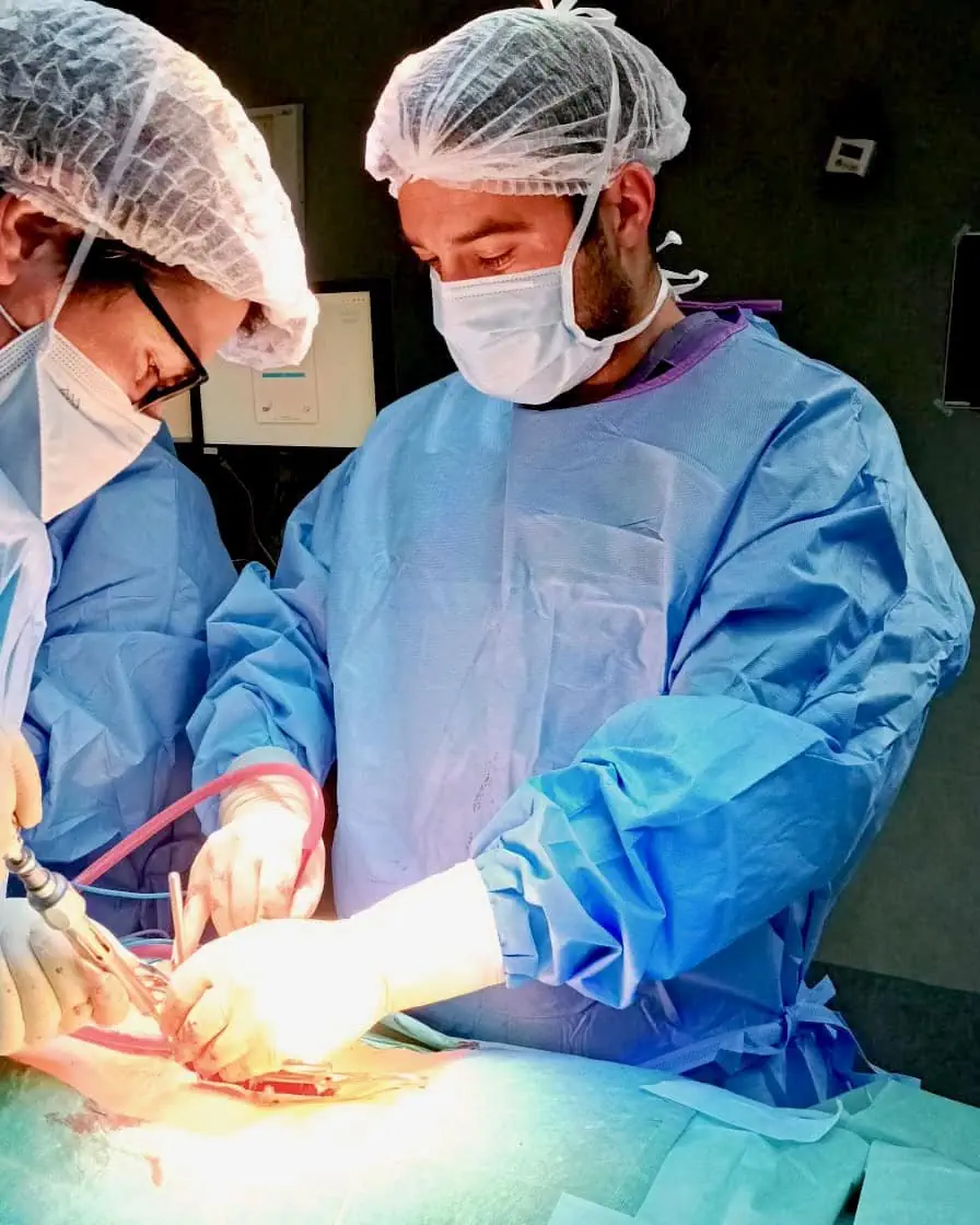 O Dr. Rafael Portela realiza uma cirurgia de revisão da coluna vertebral no bloco operatório, focado no campo cirúrgico de alta complexidade com o auxílio da sua equipa.